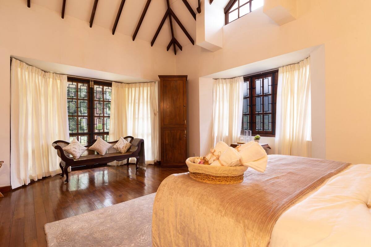 A spacious bedroom with a large bed, a wooden wardrobe, and a bench with cushions.