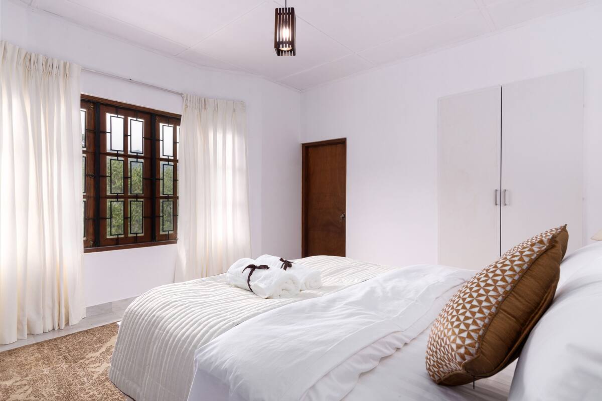 A hotel room with a bed, a wardrobe, a window with curtains, and a door.