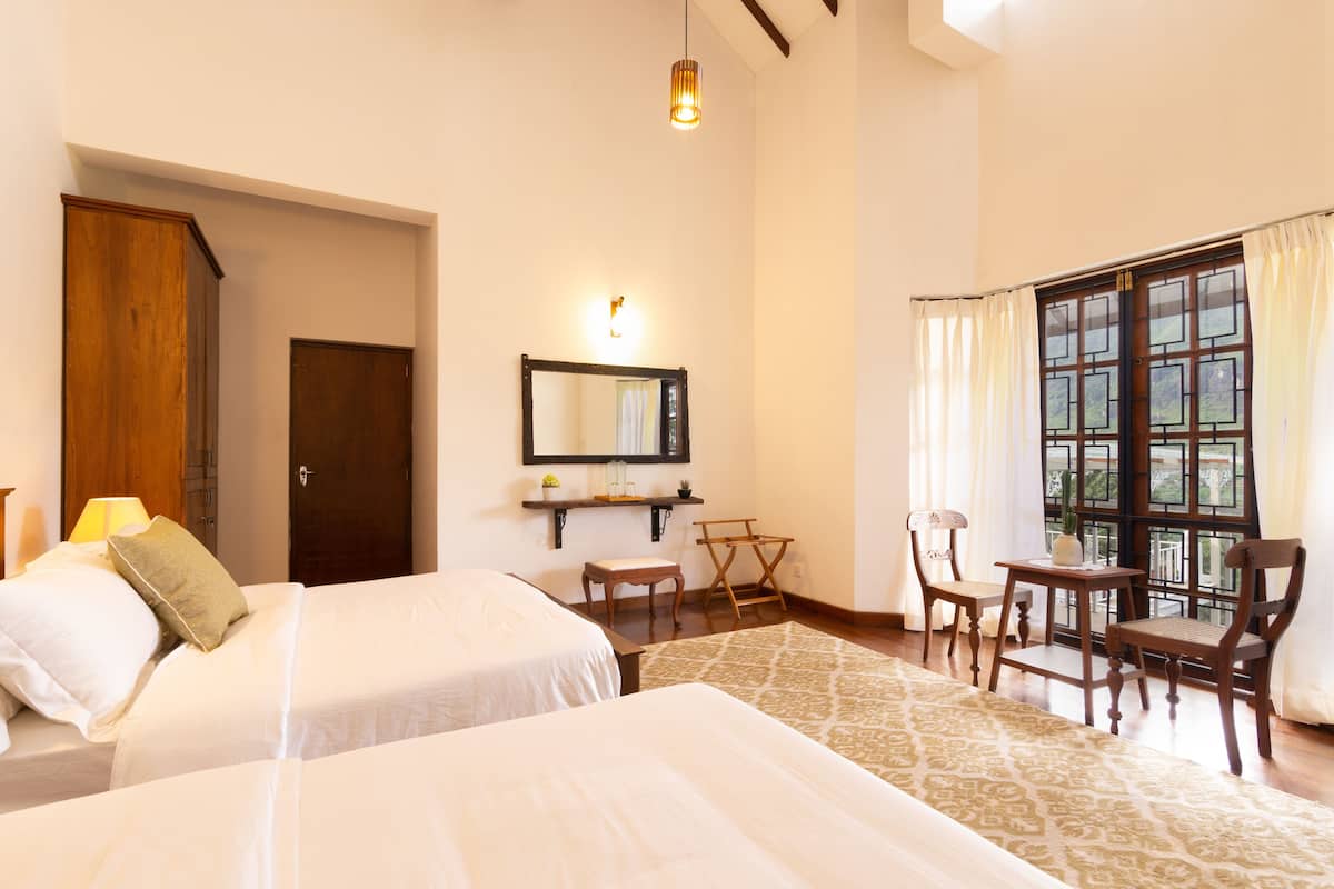 A hotel room with two beds, a sitting area with chairs, a table, a mirror, and a window with curtains.