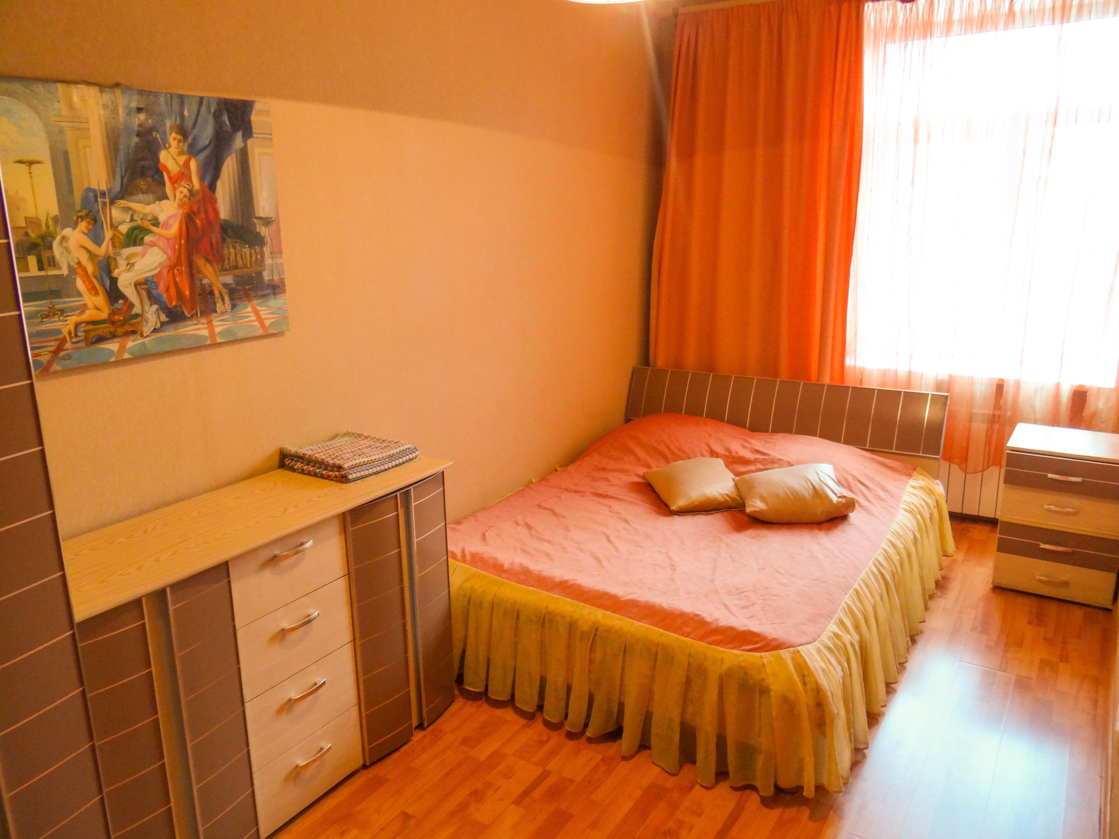 A bedroom with a bed, a desk with drawers, a painting on the wall, and a window with curtains.