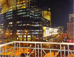 Un paisaje urbano nocturno con un edificio destacado que presenta líneas verticales iluminadas y varios pisos.