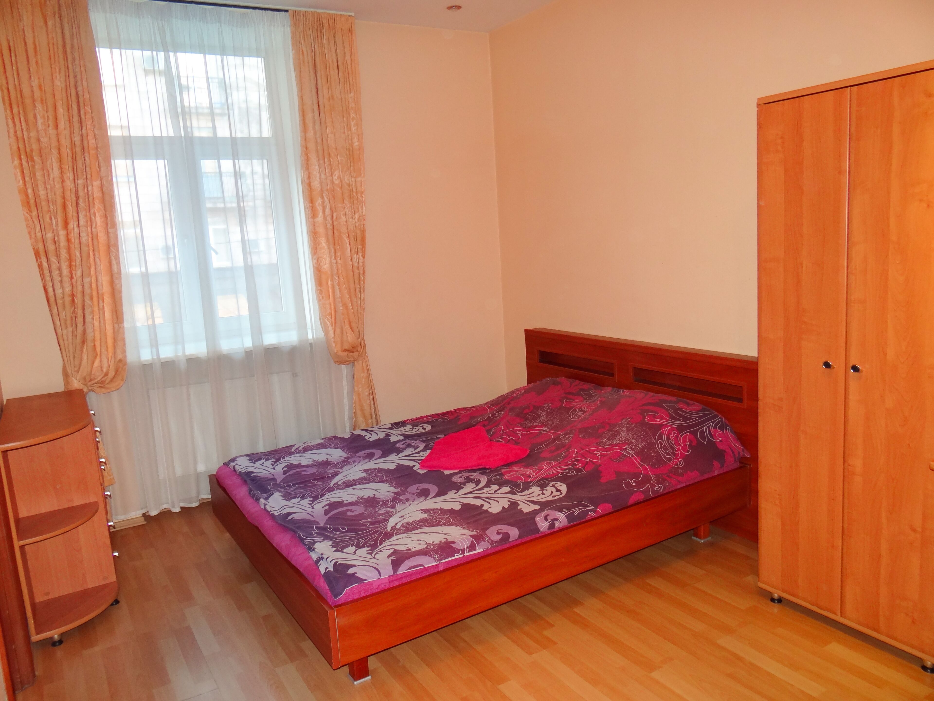 A bedroom with a wooden bed, a wardrobe, and a window with curtains.