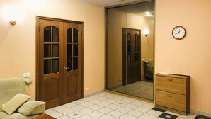 Une pièce avec une porte en bois, un miroir, une horloge, un canapé et un petit meuble en bois.