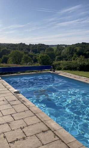 A rectangular swimming pool with clear blue water, surrounded by a paved deck.