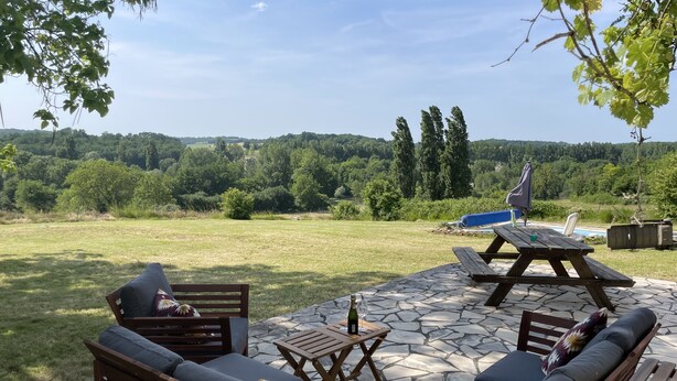 An outdoor patio with stone flooring, wooden furniture, and a view of a lush green landscape. - Renovated farmhouse with stunning views & heated pool (Verteillac)