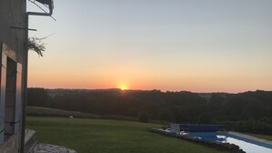 A sunset view from a building with a stone pathway leading to a swimming pool. - Renovated farmhouse with stunning views & heated pool (Verteillac)