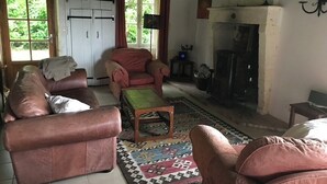 A cozy living room with leather sofas, a patterned rug, a fireplace, and a large window with curtains. - Renovated farmhouse with stunning views & heated pool (Verteillac)