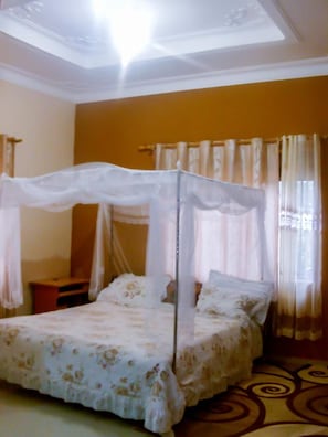 A four-poster bed with a canopy, a bedside table, and curtains. - Naju Home Stay (Masindi)