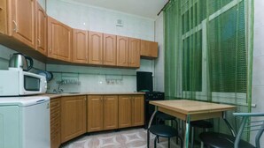 A compact kitchen with wooden cabinets, a microwave, a stove, and a dining table with chairs. - KyivHome at Khreschatyk (Kyiv)