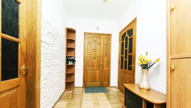 A hallway with wooden doors, a white textured wall, and a wooden console table with a vase of yellow flowers. - KyivHome at Khreschatyk (Kyiv)