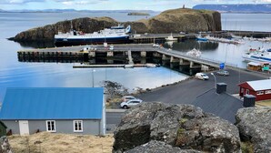 A coastal harbor with a large ferry docked at the pier, a small island with a lighthouse, and a clear view of the sea. - The Crib Rocks (Borgarnes)