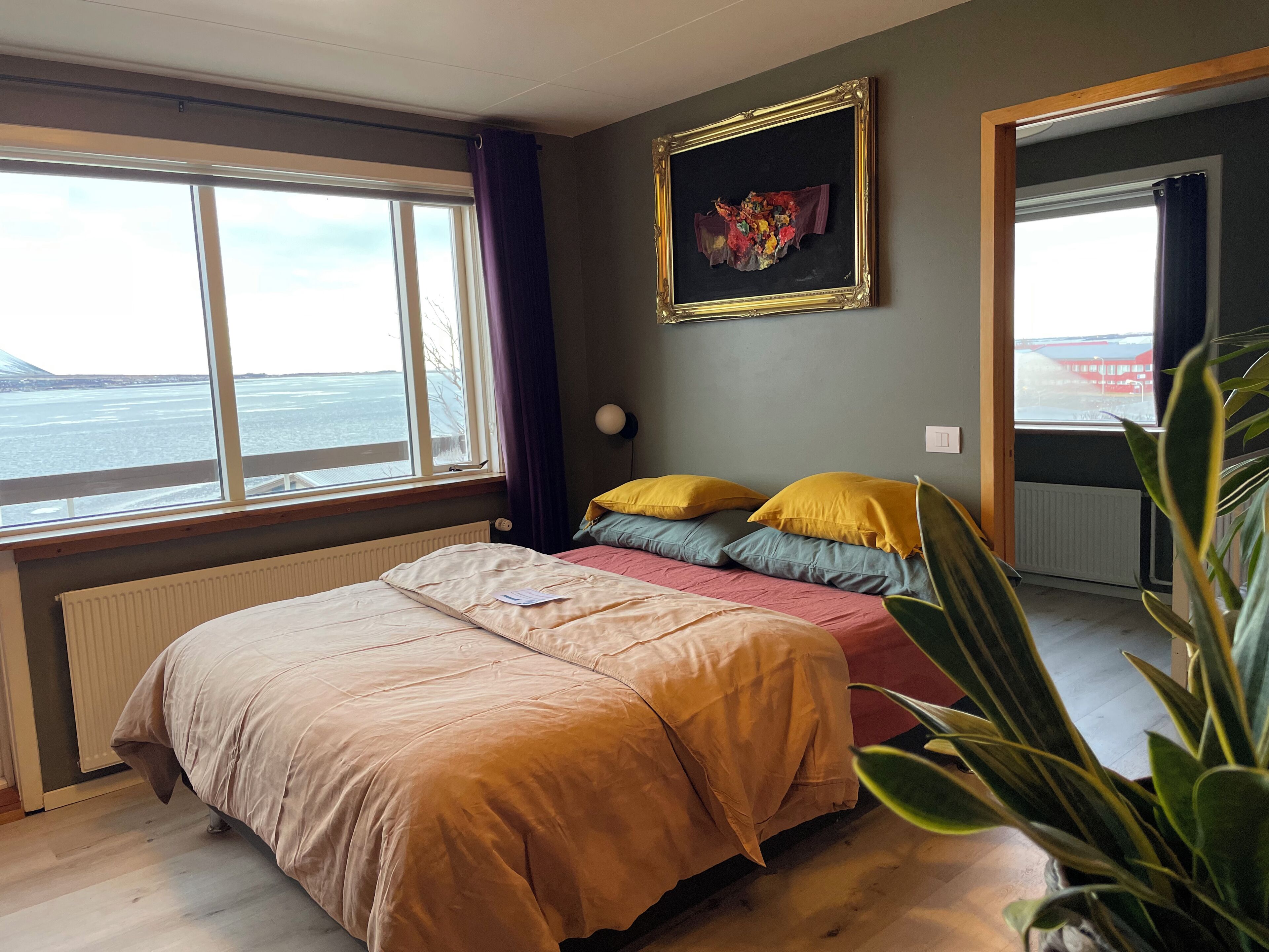 A bedroom with a bed, a window with a view, a framed artwork, and a radiator.