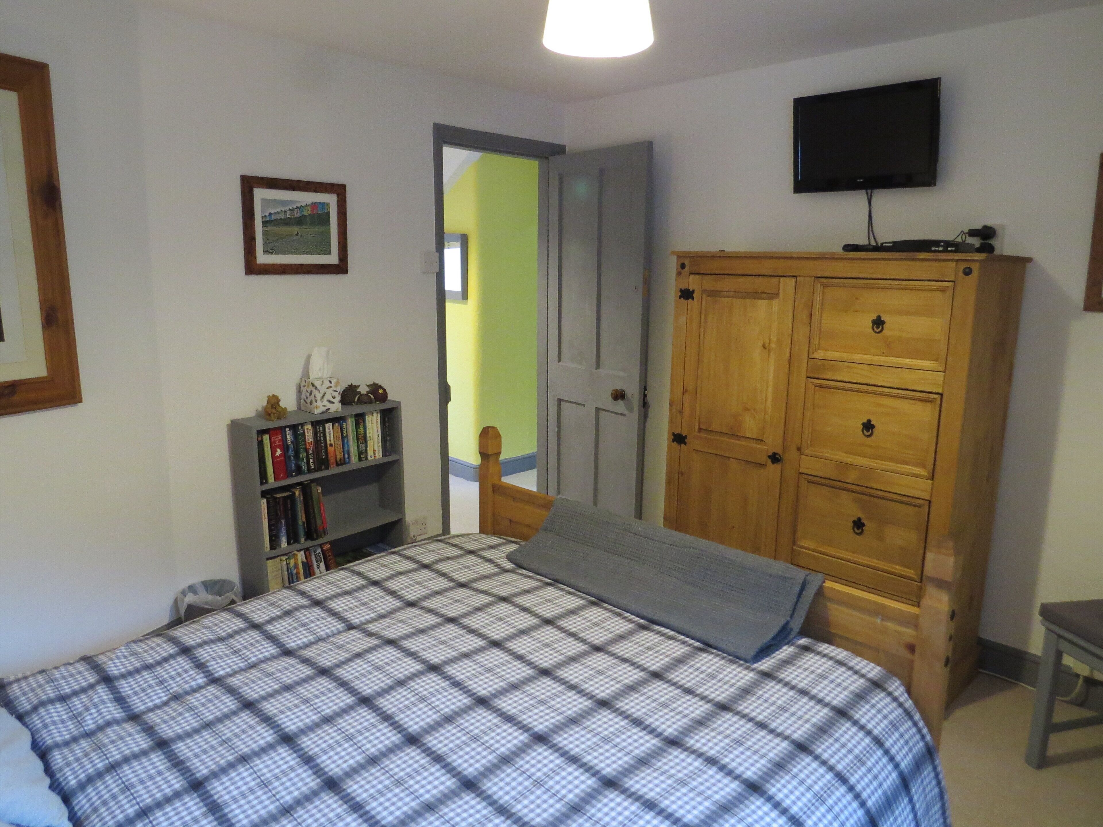 A bedroom with a bed, a wooden wardrobe, a bookshelf, a television, and a door leading to another room.