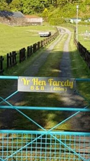Une route de campagne avec un panneau indiquant « Yr Hen Farcody, chambre d’hôtes (400 m) ».