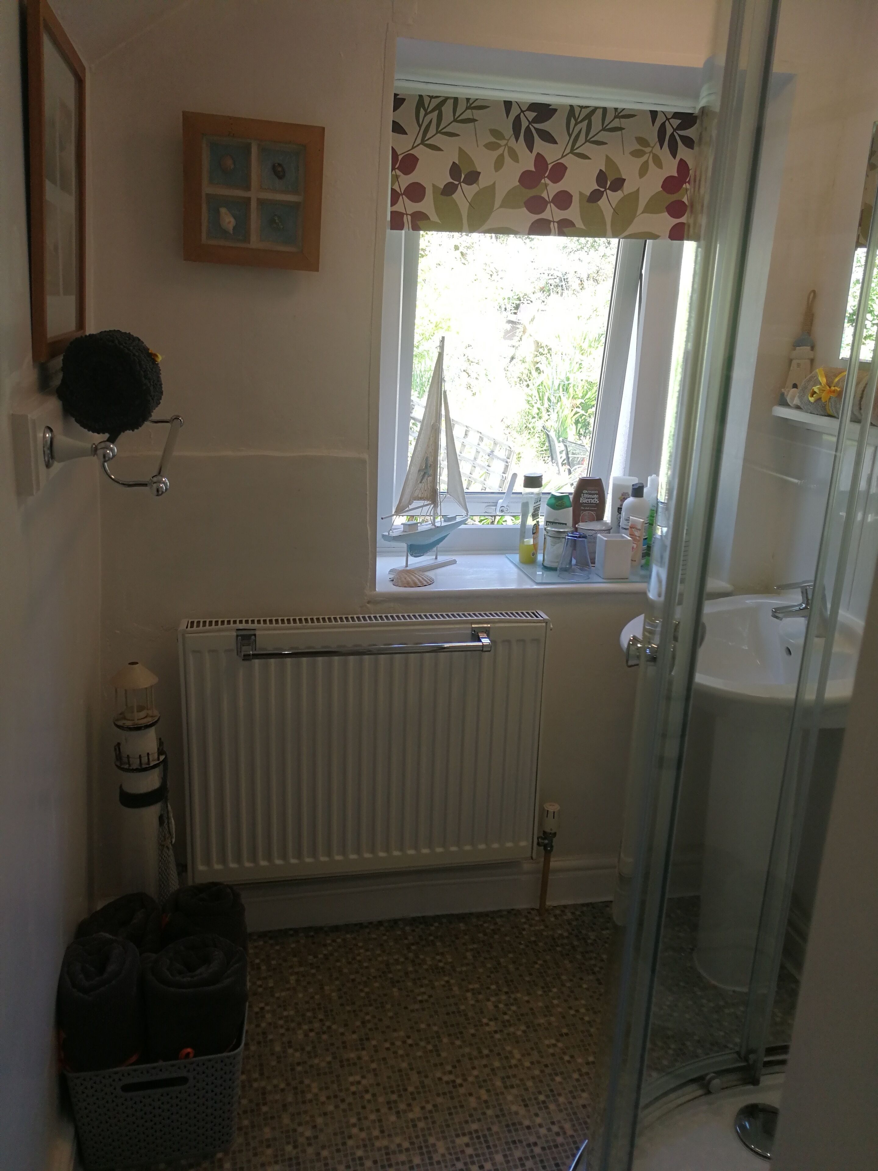 Un baño con ventana, radiador, una pequeña decoración de velero y cabina de ducha de vidrio.