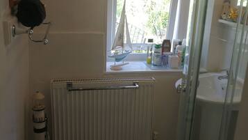 Un baño con ventana, radiador, una pequeña decoración de velero y cabina de ducha de vidrio.