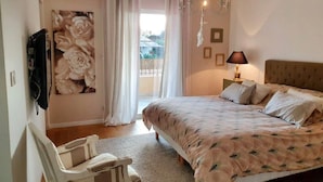 A bedroom with a bed, a chair, a lamp, a chandelier, and a painting of flowers. - Villa "Chjosella" (Santa Reparata di Balagna)