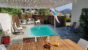 A poolside area with a wooden table, lounge chairs, and a hanging chair. - Villa "Chjosella" (Santa Reparata di Balagna)