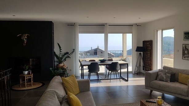 A spacious living room with a sofa, dining table, and chairs. There is a balcony with a view of the city. - Villa "Chjosella" (Santa Reparata di Balagna)
