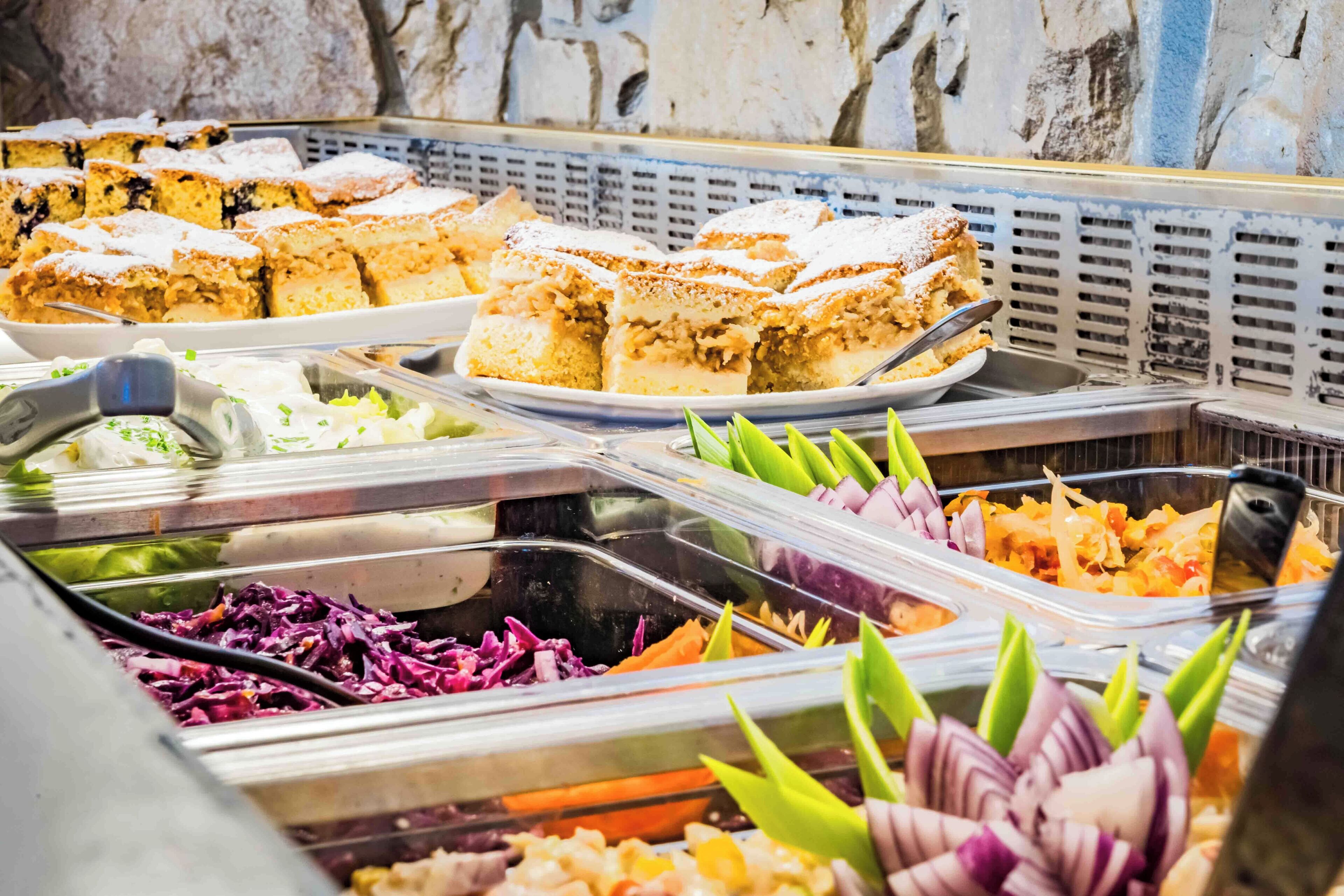 Ein Buffet mit verschiedenen Speisen, darunter Krautsalat, gemischtes Gemüse und eine Auswahl an Brownies.