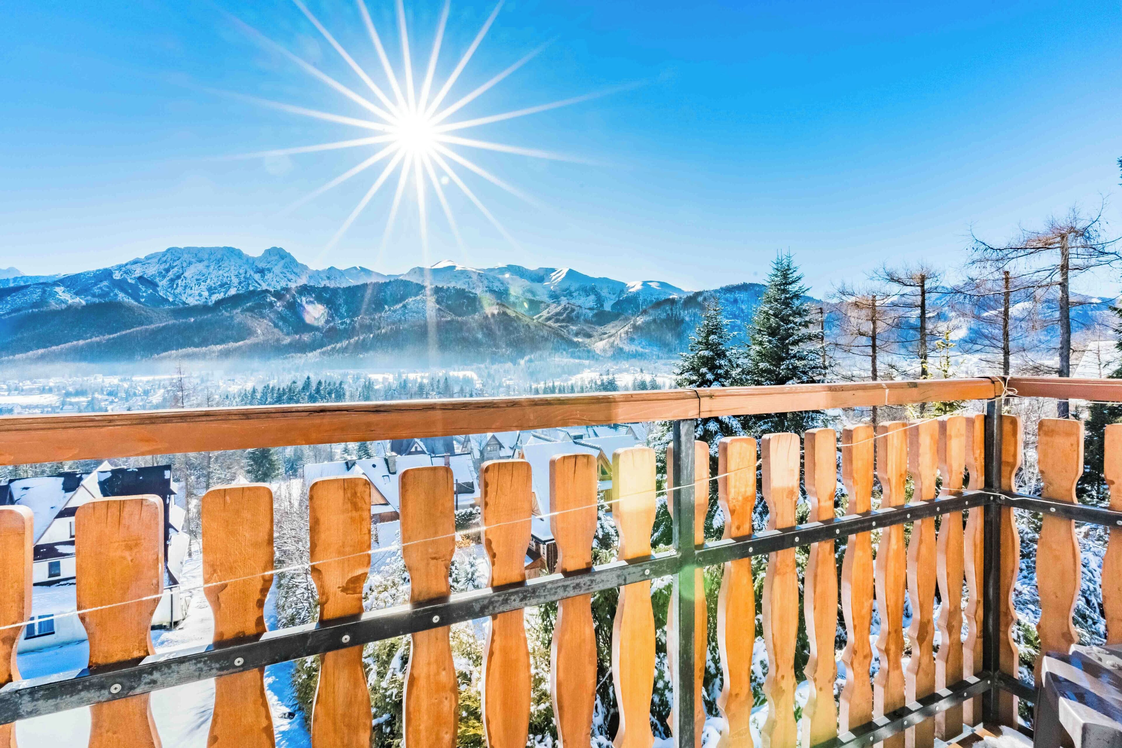 Barandilla de madera con vistas a un paisaje montañoso nevado bajo un cielo despejado.