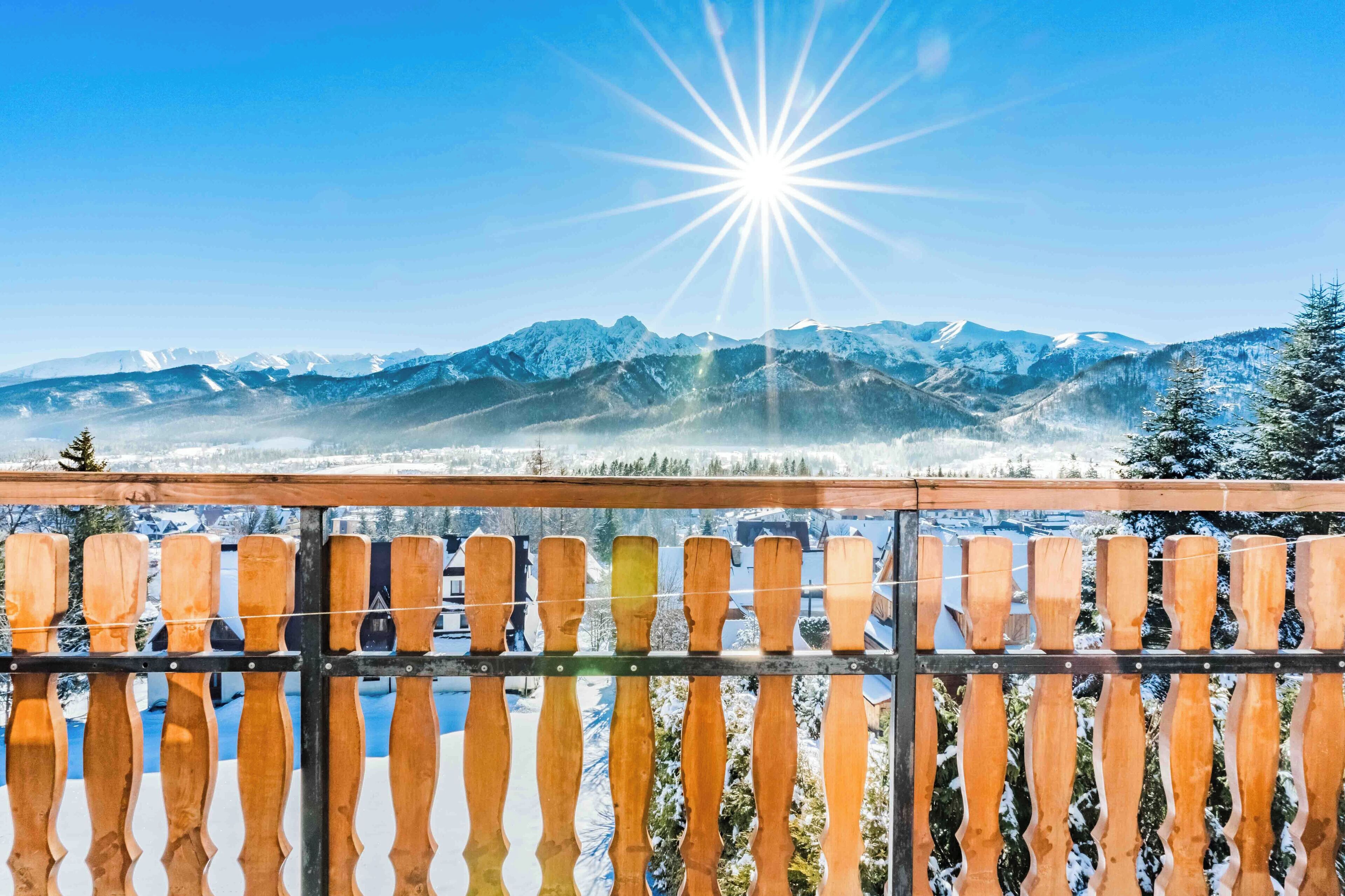 A balcony with a view of snow-covered mountains and a bright sun.