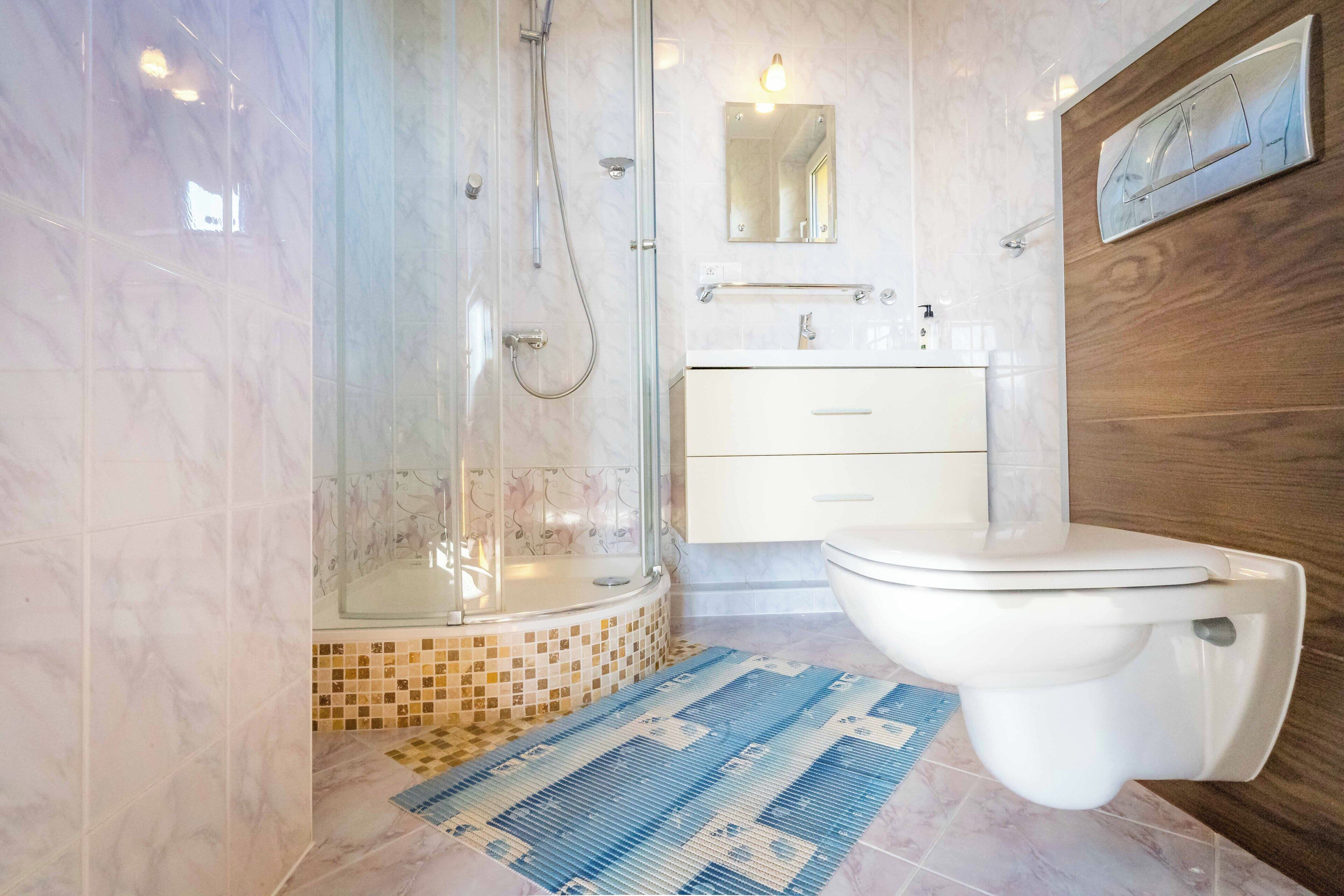 A modern bathroom with a glass-enclosed shower, a white toilet, a wooden vanity, and a tiled floor.