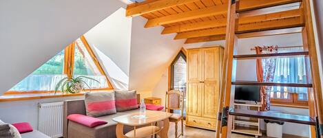 Un dormitorio estilo loft acogedor, con techo inclinado, escalera de madera, sofá, mesa y televisor.