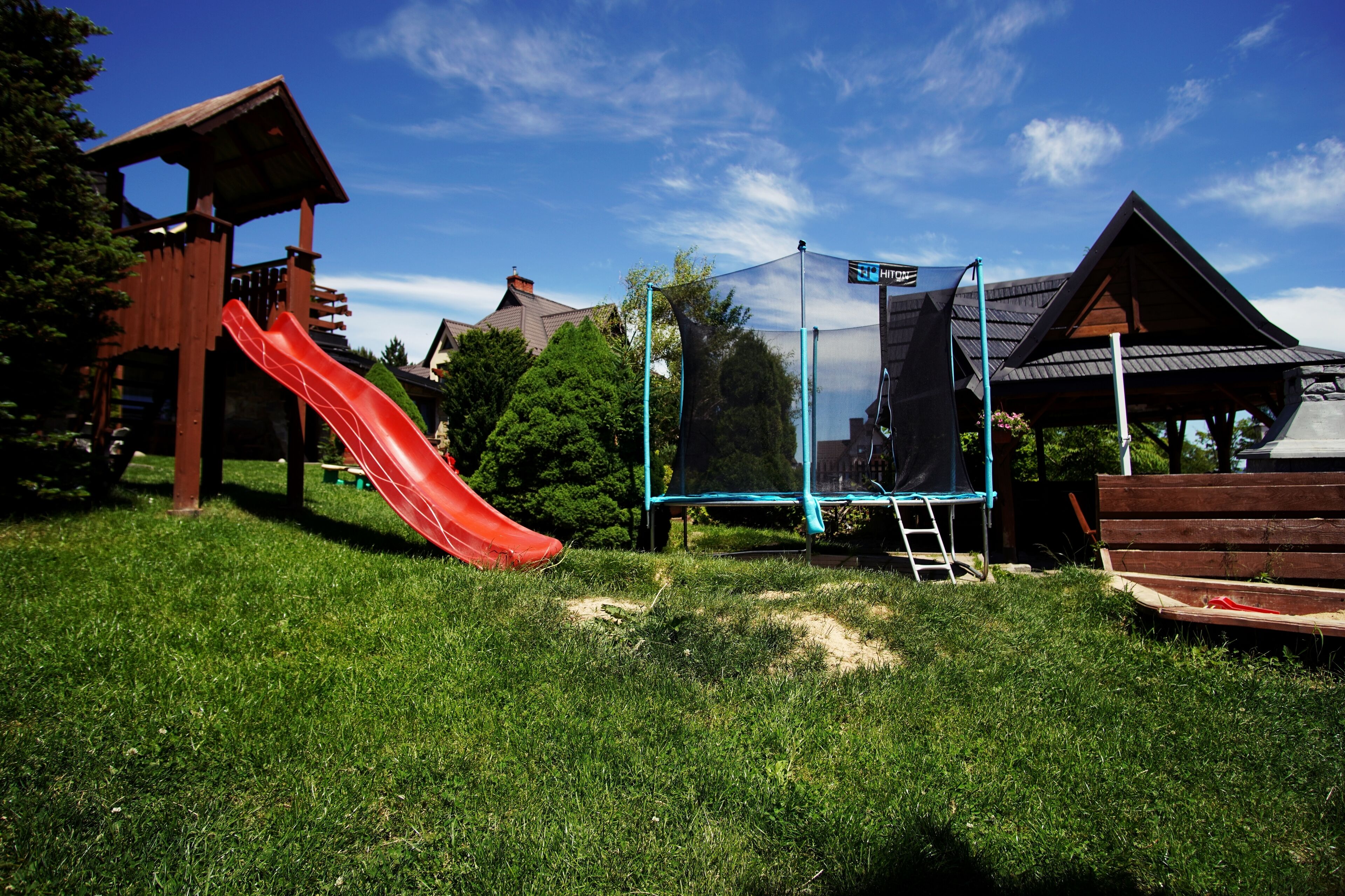 A playground with a red slide, a trampoline, and a wooden playhouse.