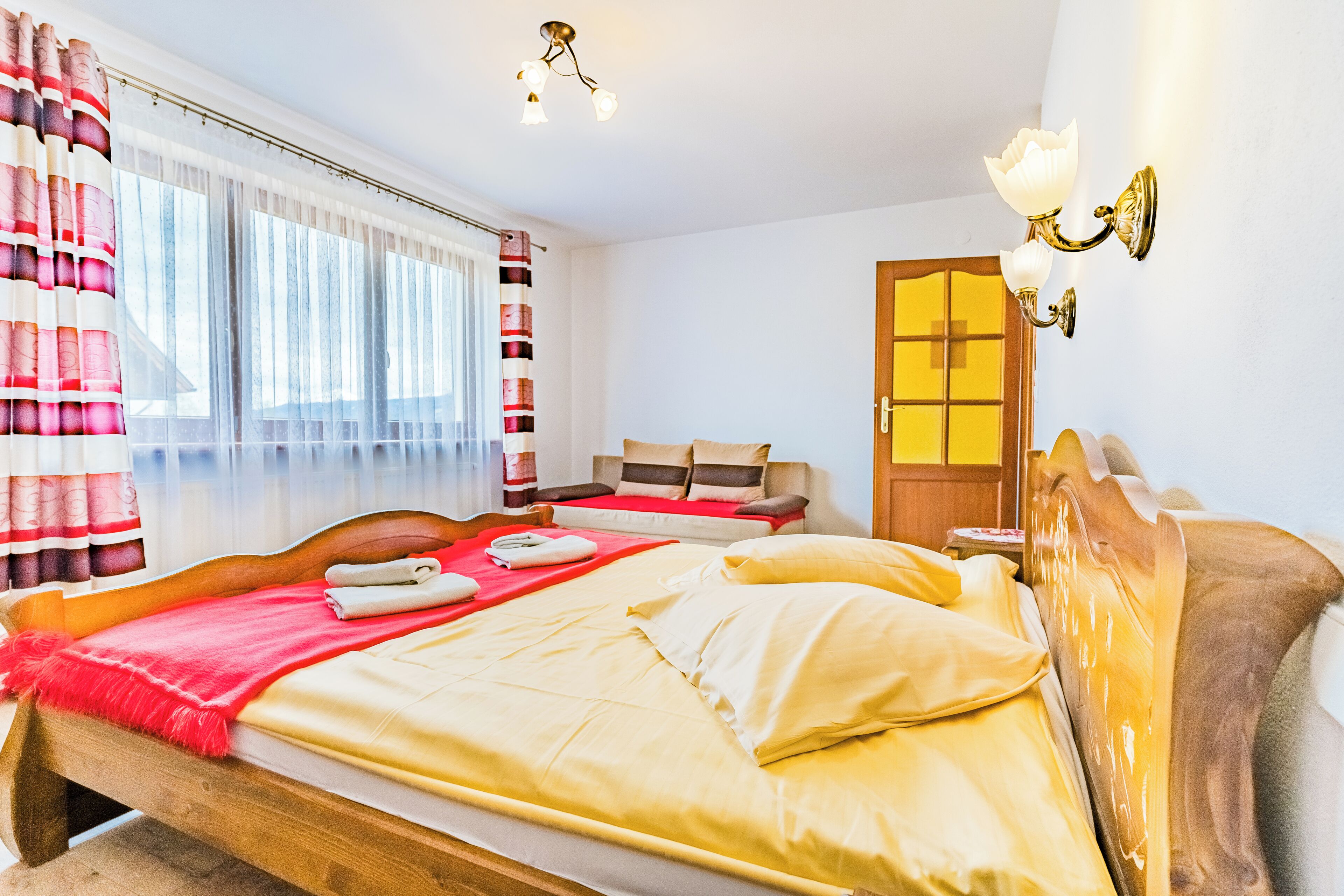 Une chambre d’hôtel avec un lit en bois, un rideau à rayures rouges et blanches, une tête de lit en bois et un luminaire fixé au mur.