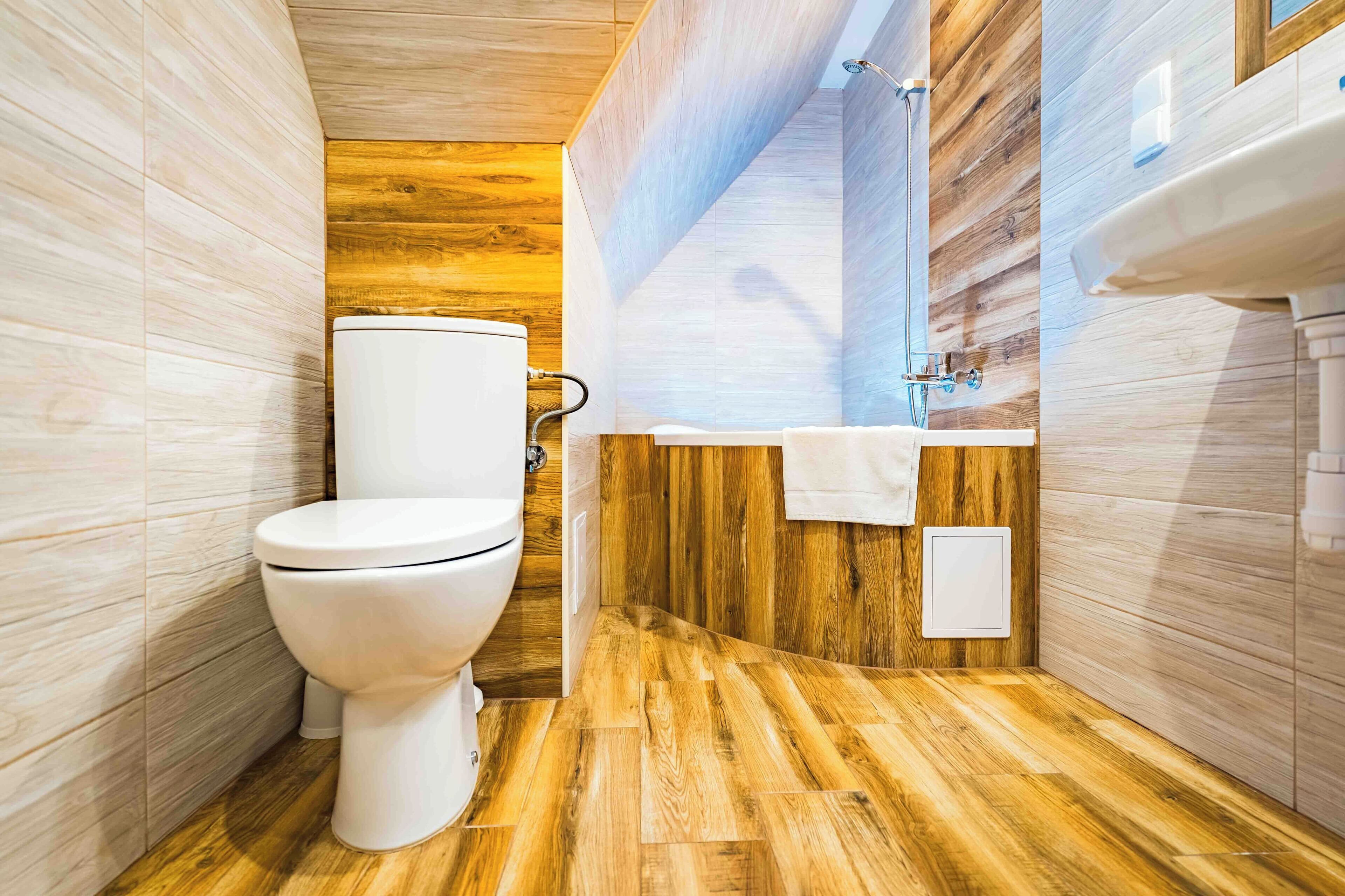 Un bagno moderno con pavimento in legno, un water bianco e un lavabo con uno specchio sopra.