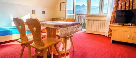 A room with a dining table, chairs, a TV, and a view of mountains through large windows.