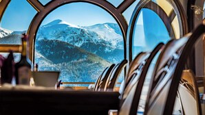 Vista desde la ventana de una cabaña con un paisaje montañoso cubierto de nieve.