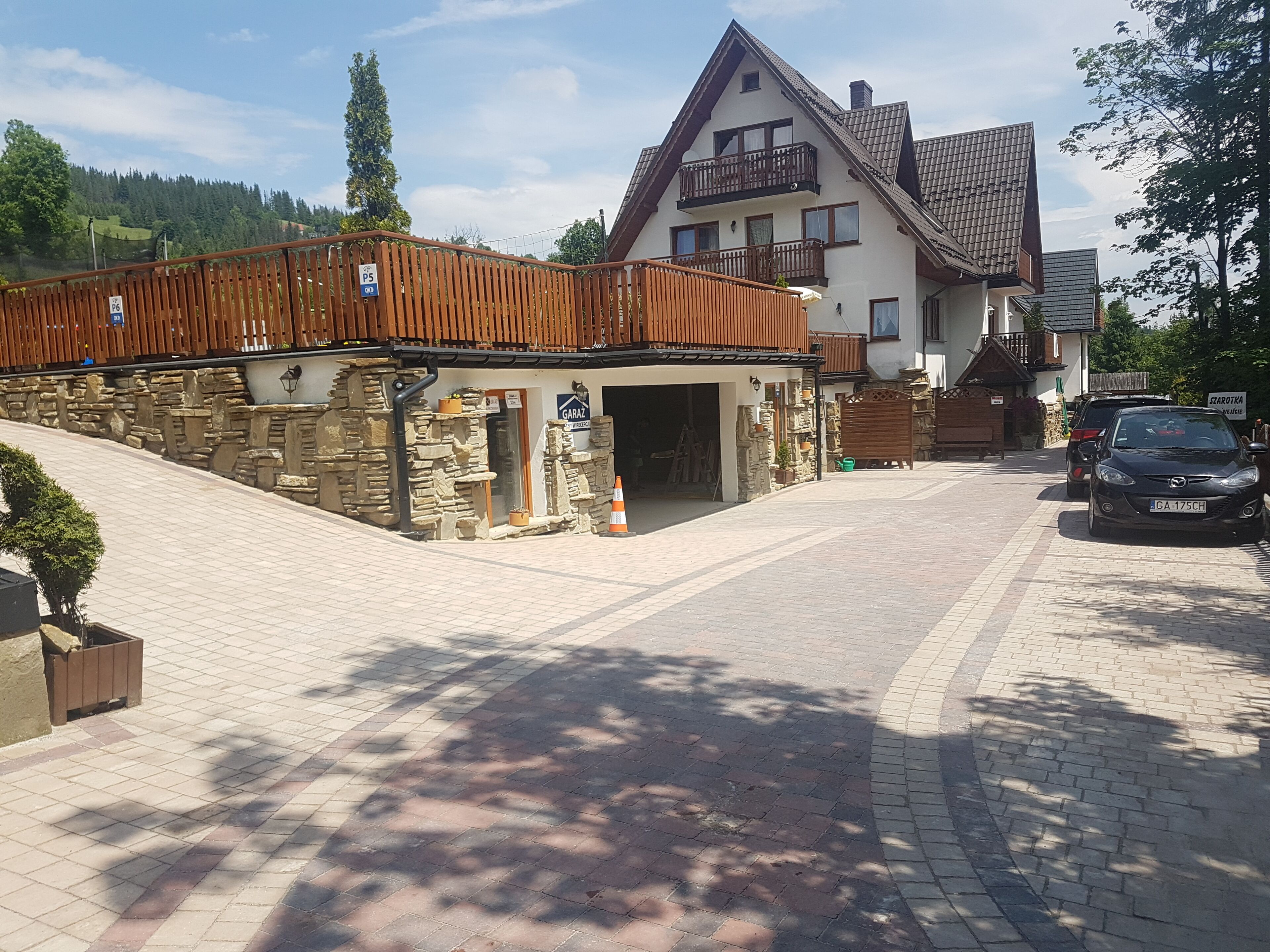 Een stenen gebouw met een houten terras, een garage en een auto ervoor geparkeerd.
