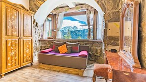 Una habitación acogedora con pared de piedra, un armario de madera, un sofá con cojines y una ventana con vistas a la montaña.