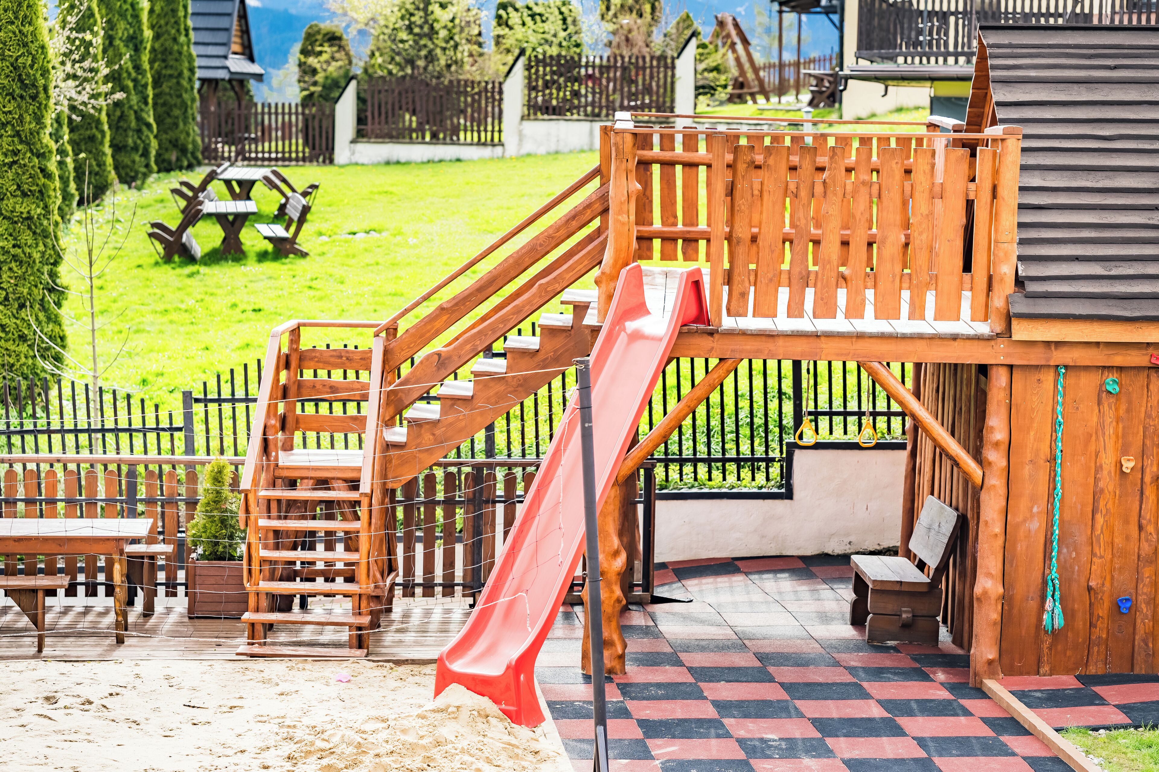 A wooden play structure with a slide, a picnic table, and a checkered floor.