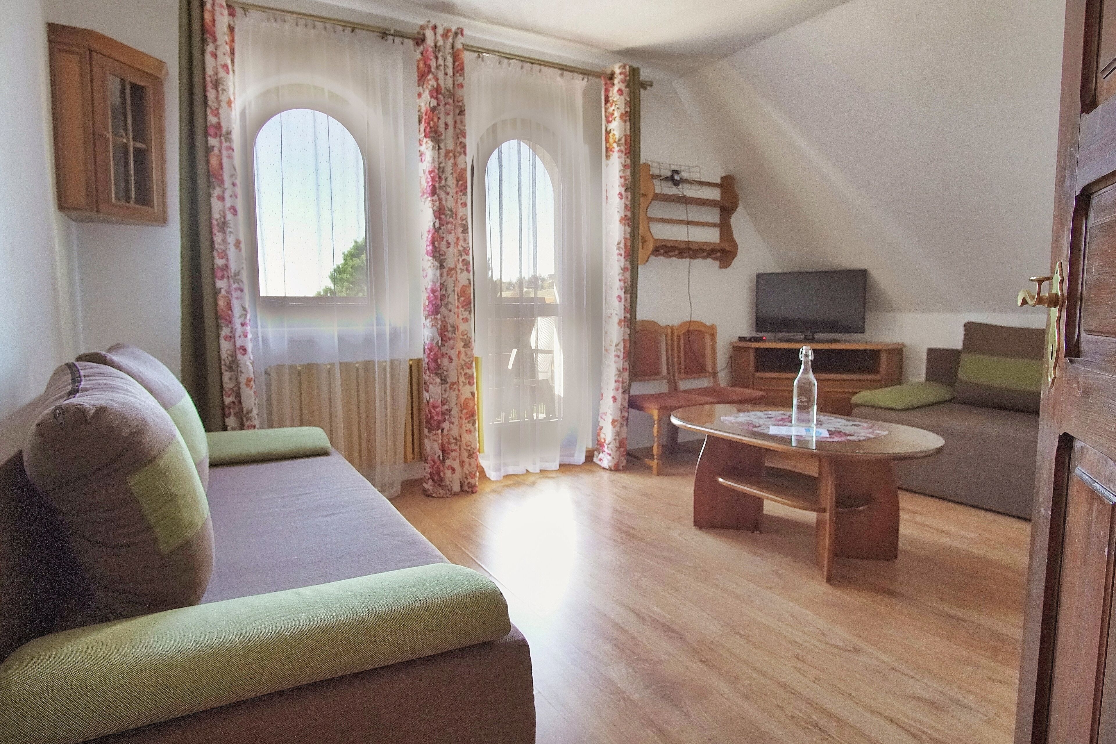 Ein gemütliches Wohnzimmer mit einer Couch, einem Holztisch und einem Fernseher auf einem Standfuß.
