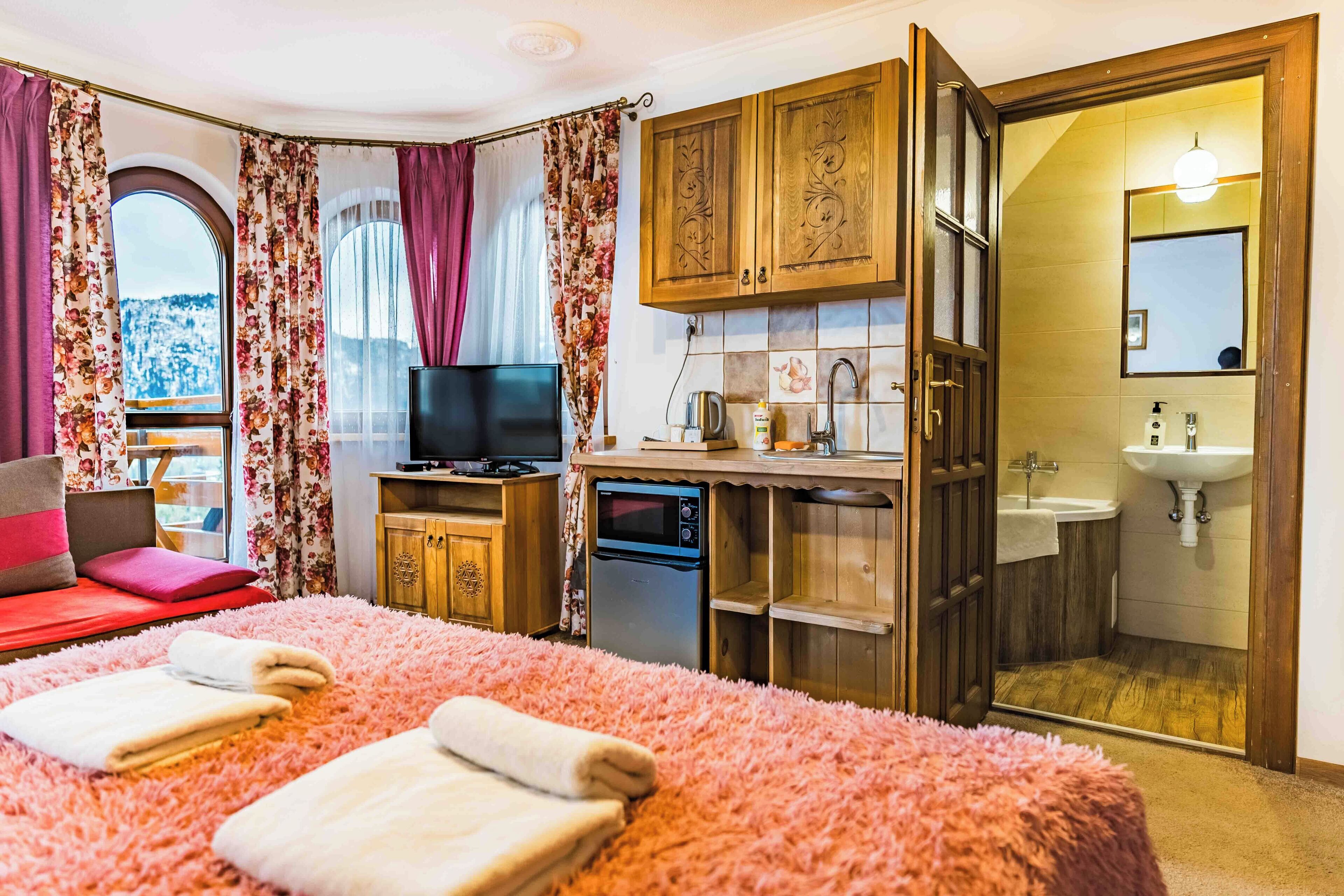 Una camera da letto con un ampio letto, una TV, una scrivania con un computer e un bagno con lavandino e specchio.