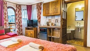 Un dormitorio con una cama grande, televisión, escritorio con computadora y baño con lavamanos y espejo.