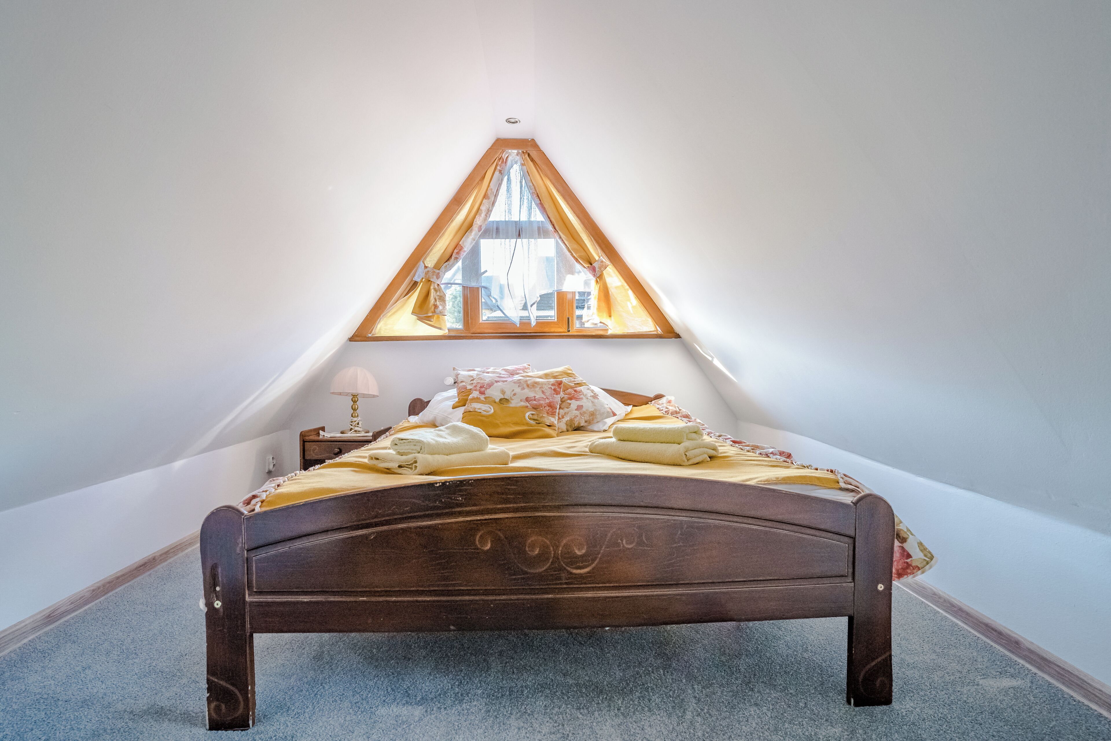 Ein Schlafzimmer mit einem hölzernen Bett, einem dreieckigen Fenster und einem Nachttisch mit Lampe.