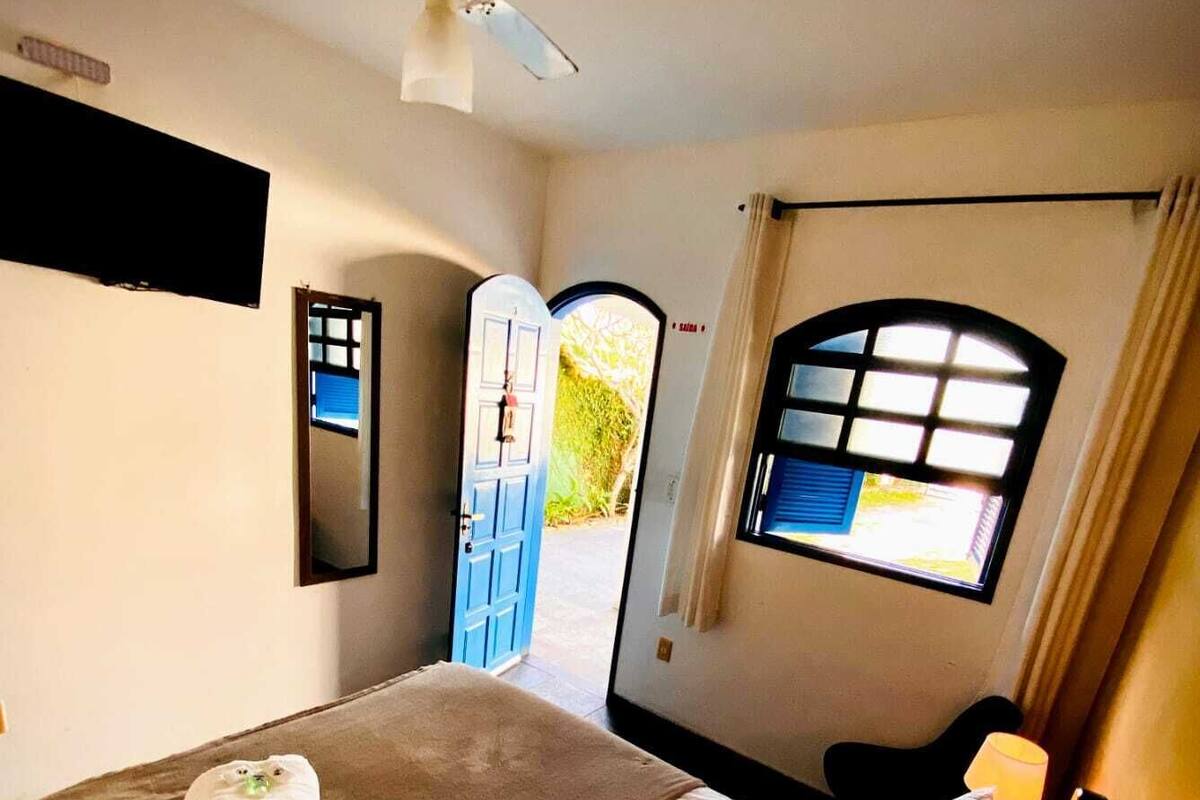 Une chambre d’hôtel avec un lit, une fenêtre avec des rideaux, une porte et un ventilateur de plafond.