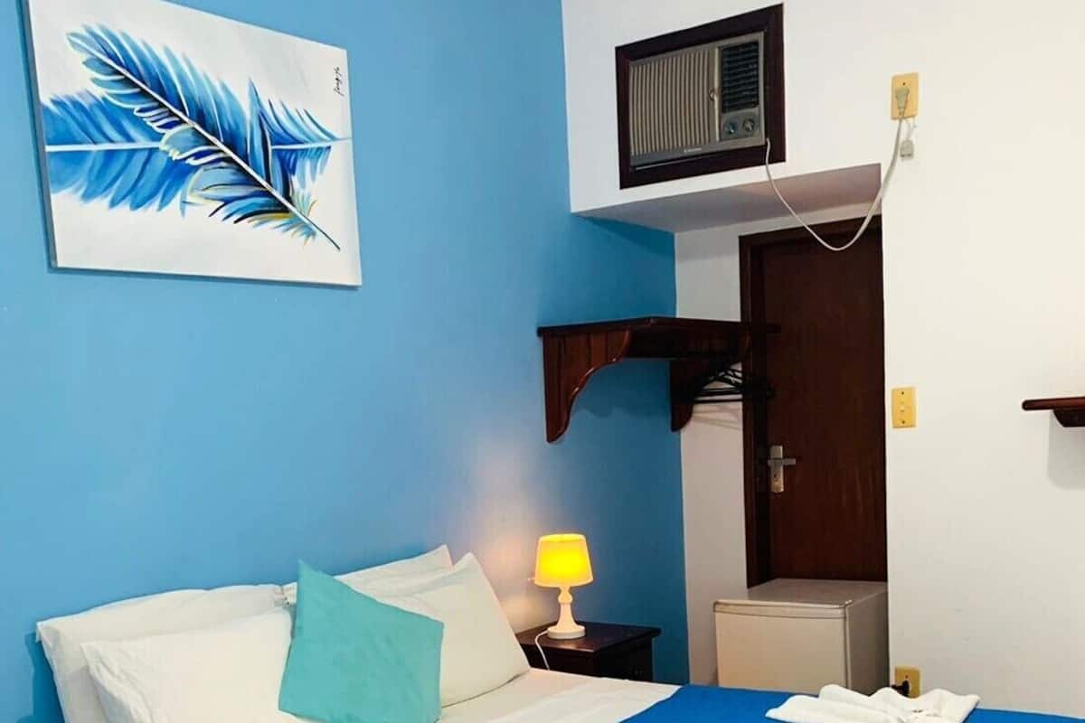 Une chambre d’hôtel avec un lit, une table de chevet, une lampe, un radiateur et une porte.
