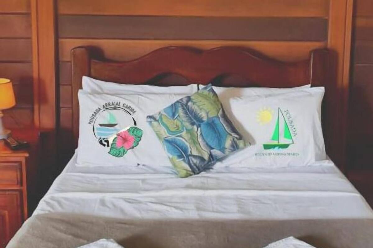Un lit avec deux oreillers : l’un est orné d’un motif représentant un voilier et un soleil, et l’autre d’un motif de feuilles tropicales.