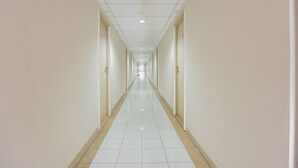 A long, narrow hallway with white tiled floors and walls, doors on both sides, and a ceiling with recessed lighting. - OYO 2103 Lauv Room 2 Grand Centerpoint Tower B (Bekasi)