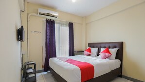 A neatly made bed with a red and white bedspread, a brown headboard, and two red pillows. There is a small table with a lamp and a power outlet on the left. An air conditioning unit is mounted on the wall above the bed. - OYO 2103 Lauv Room 2 Grand Centerpoint Tower B (Bekasi)