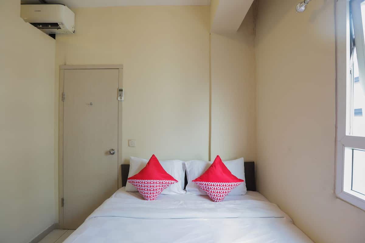 Une chambre d’hôtel avec un lit, deux oreillers à motifs rouges et blancs, une porte blanche et une fenêtre.