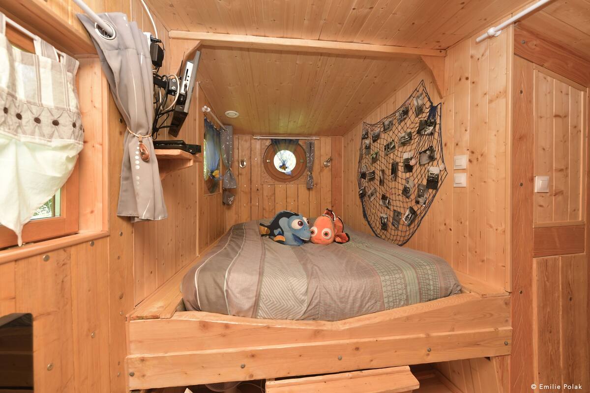 A wooden room with a bed, a window with curtains, and a wall with a netted decoration.