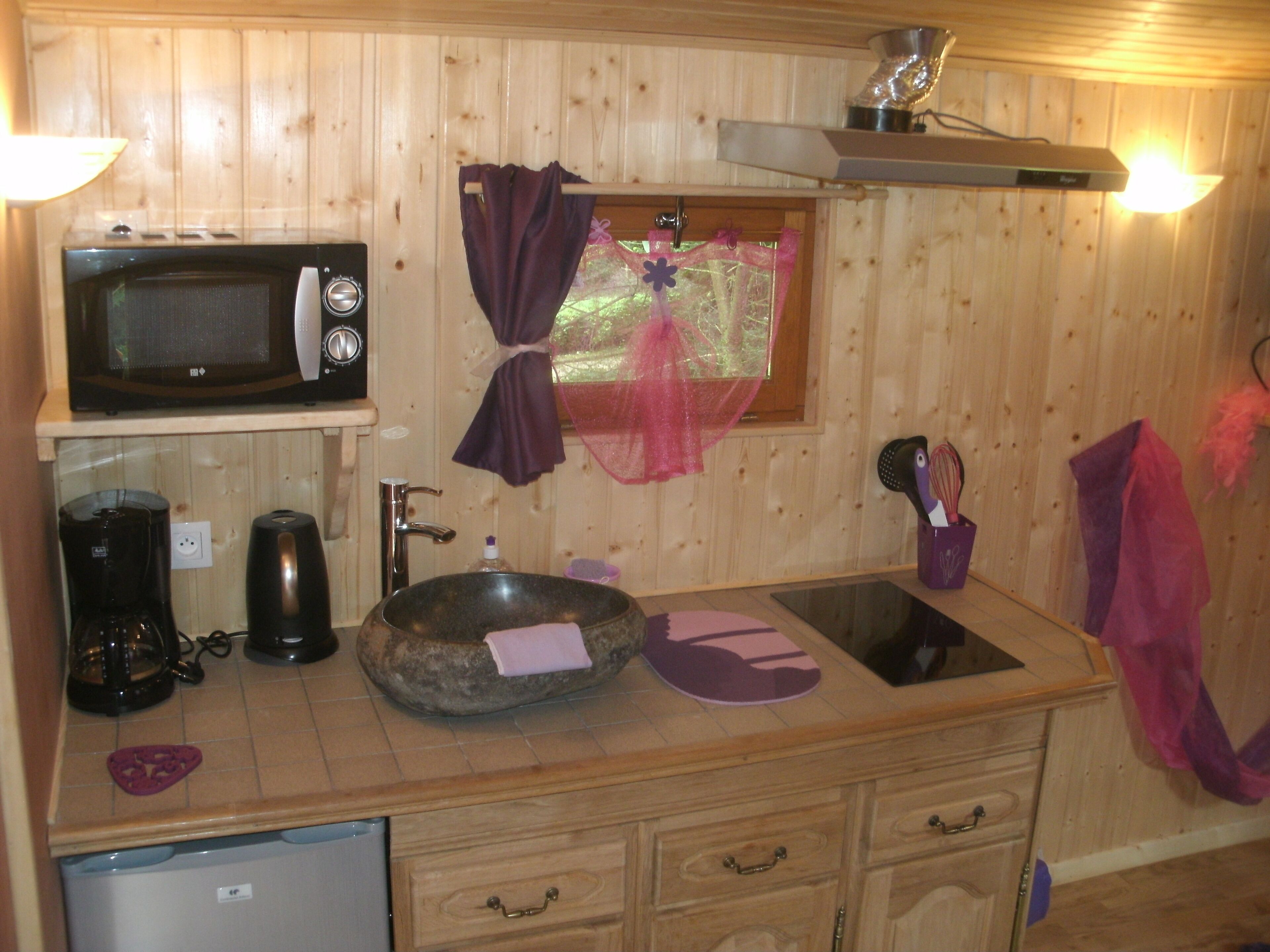 Una cocina compacta con microondas, cafetera, fregadero y armarios de madera.