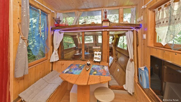 A cozy cabin interior with a wooden table, a bench, and a small boat model. - Roulotte la Verdine (Dury)