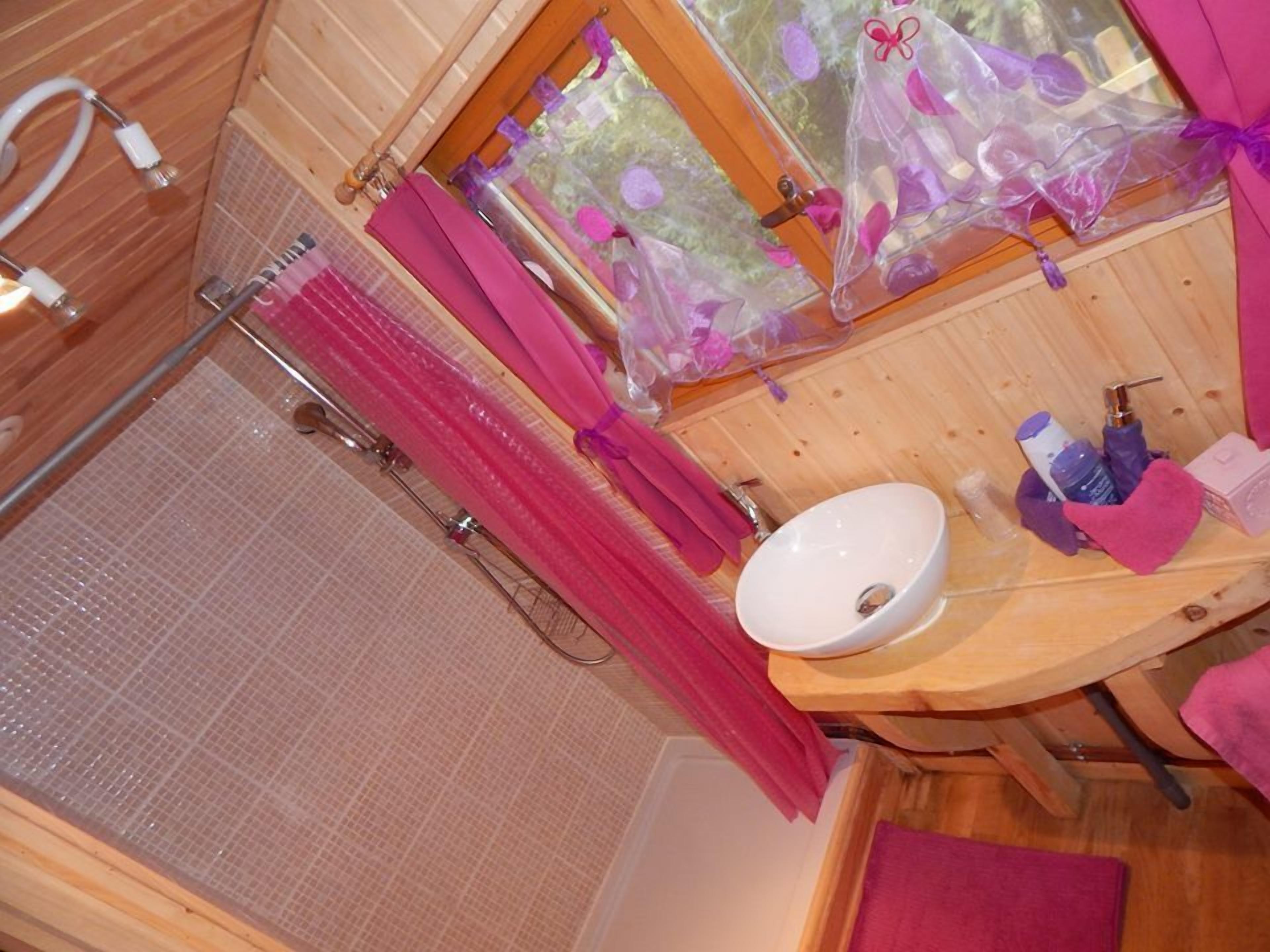 A wooden cabin bathroom with a shower, a sink, and a window with a view of flowers.
